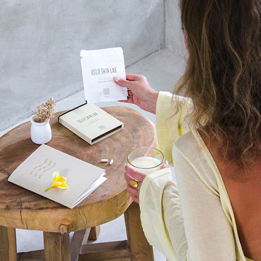 žena otočená zády ke kameře se dívá na dřevěný stůl před ní, na kterém je položené balení The Glow